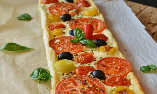 a puff pastry tart with tomato and basil on top of baking paper