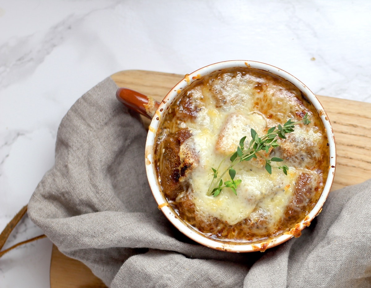 french onion soup with sprig of thyme topped with cheese on wooden board on top of kitchen counter