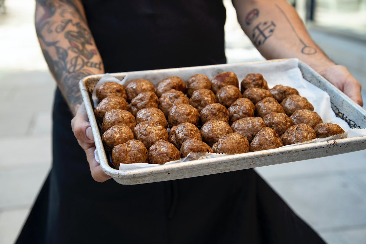 man with tattoos holding tray of meatballs - student lunch ideas