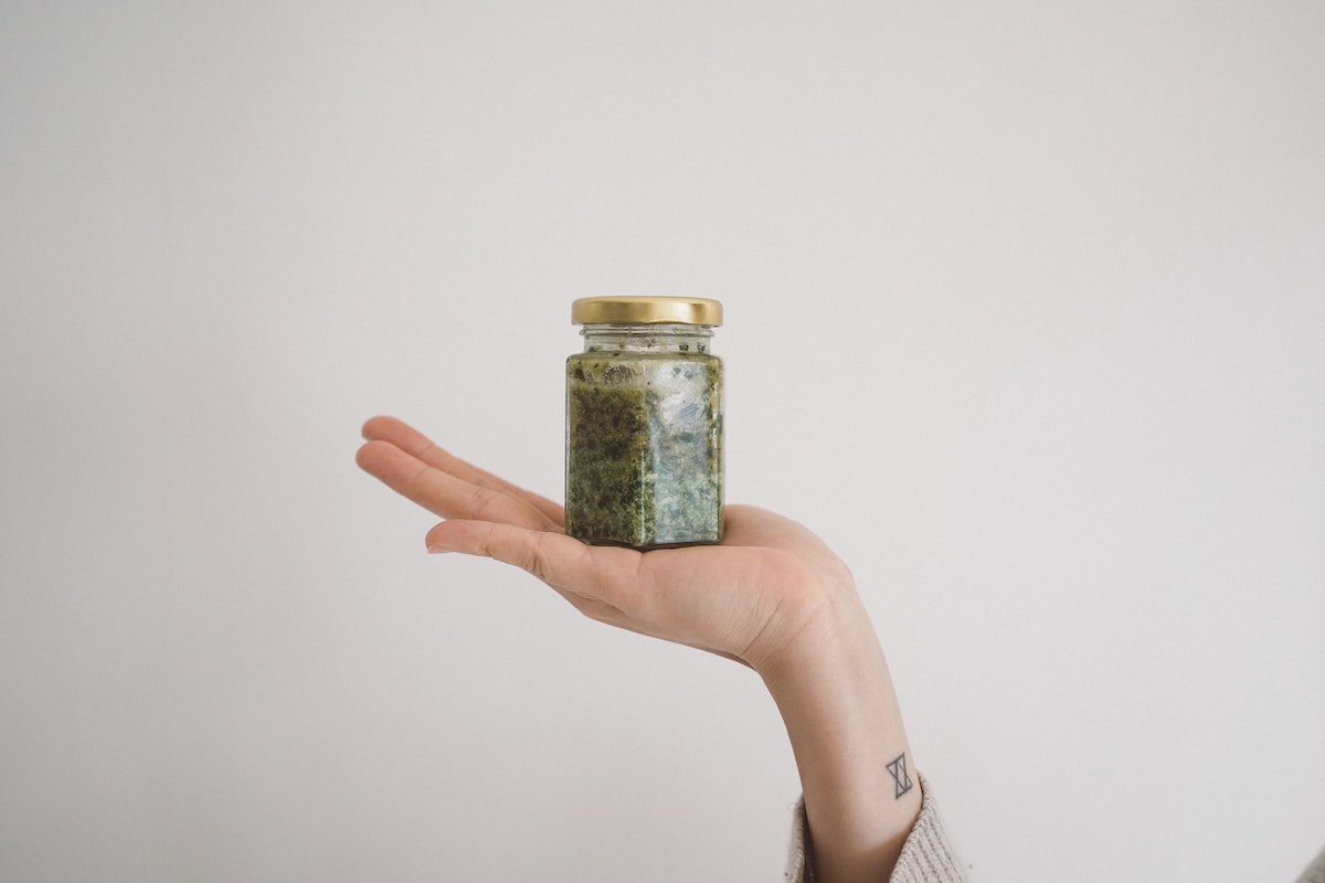 jar of green pesto held up in hand on blank background - student lunch ideas