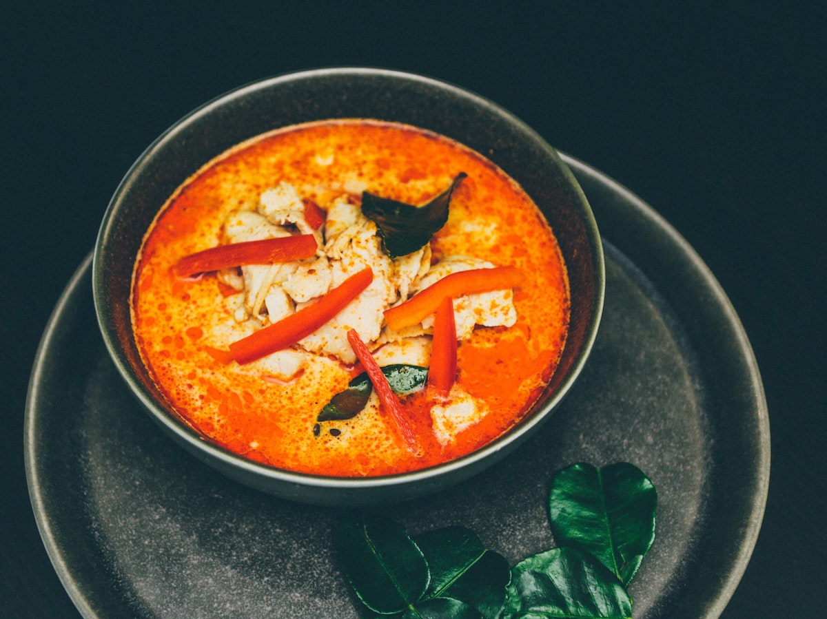 thai red curry soup with peppers and chicken on top in a dark bowl on a dark plate