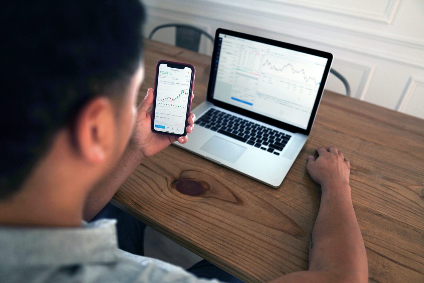 Man looking at stock trades on his phone and laptop