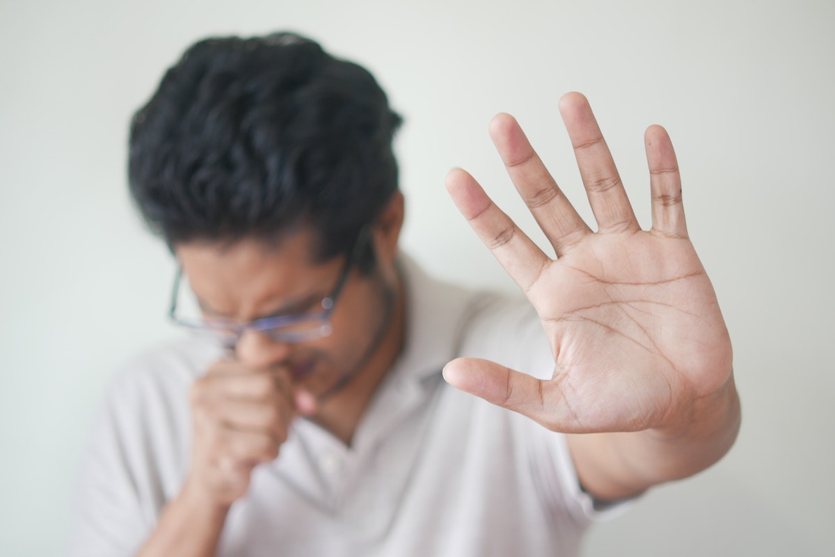 person with hay fever symptoms sneezing and sticking hand out