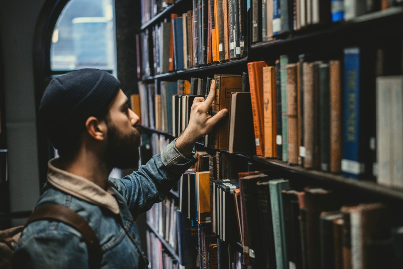 Student male in library picking a book off the shelf