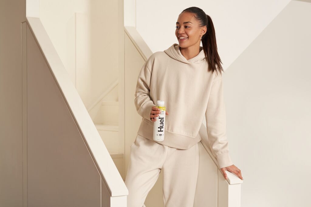 Woman wearing a hoody and joggers with a Huel ready to drink in her hand