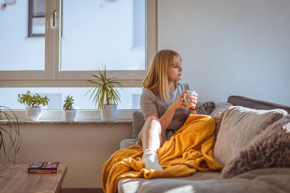 woman on couch with blanket and mug