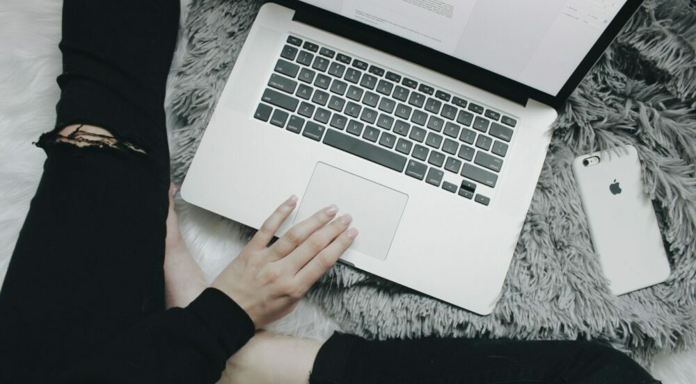 Person sat crossed legs with their hand on their open laptop